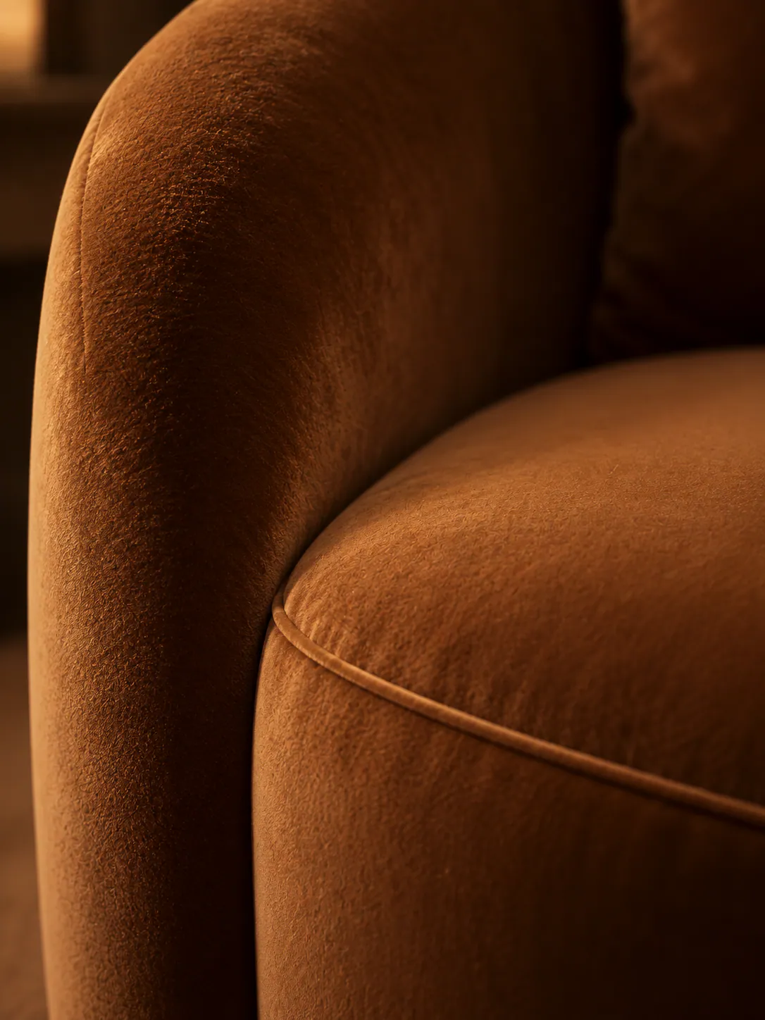The curve of a camel velvet armchair in warm, low light